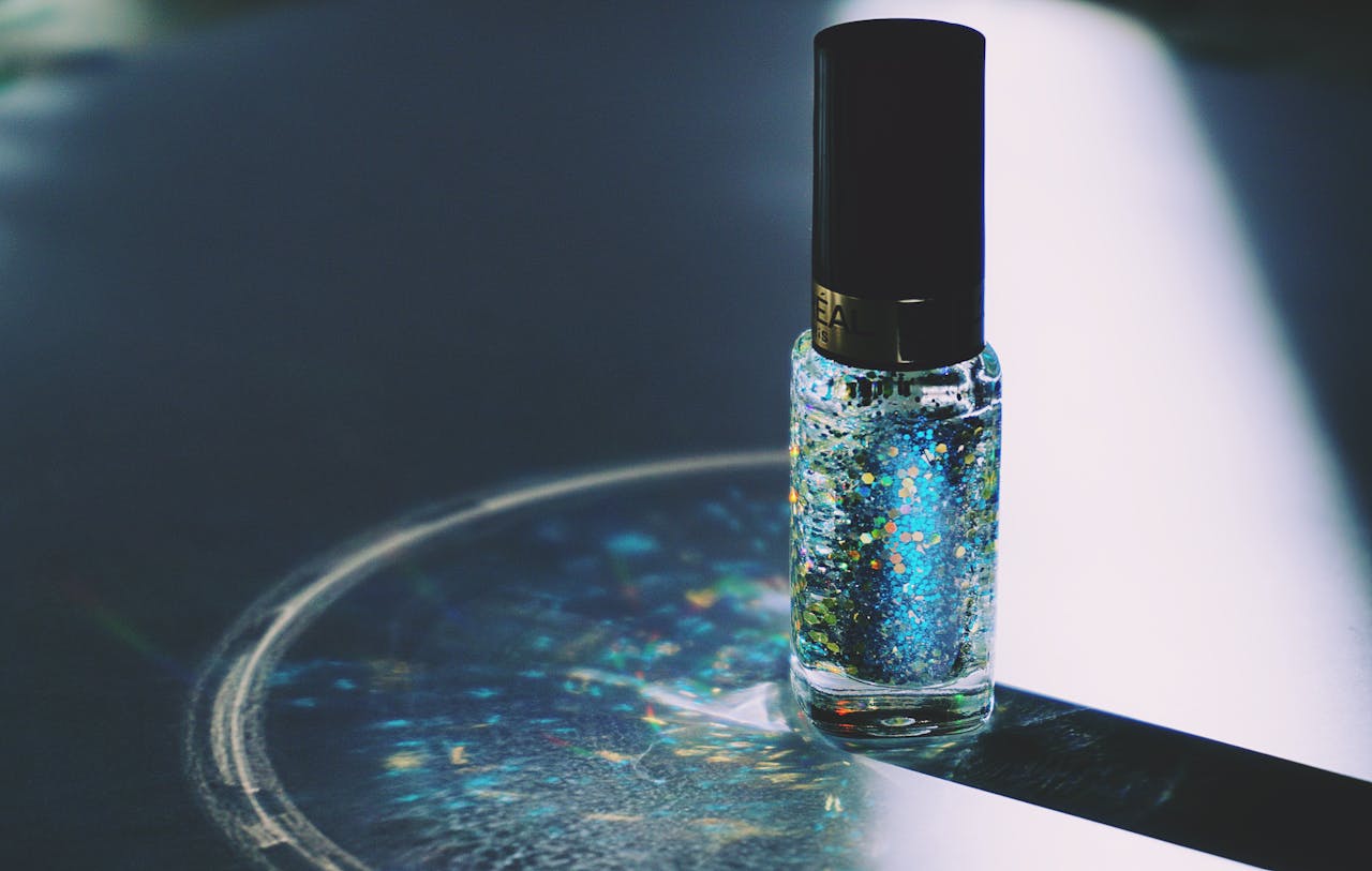 Close-up of a glitter nail polish bottle reflecting colors on a surface.